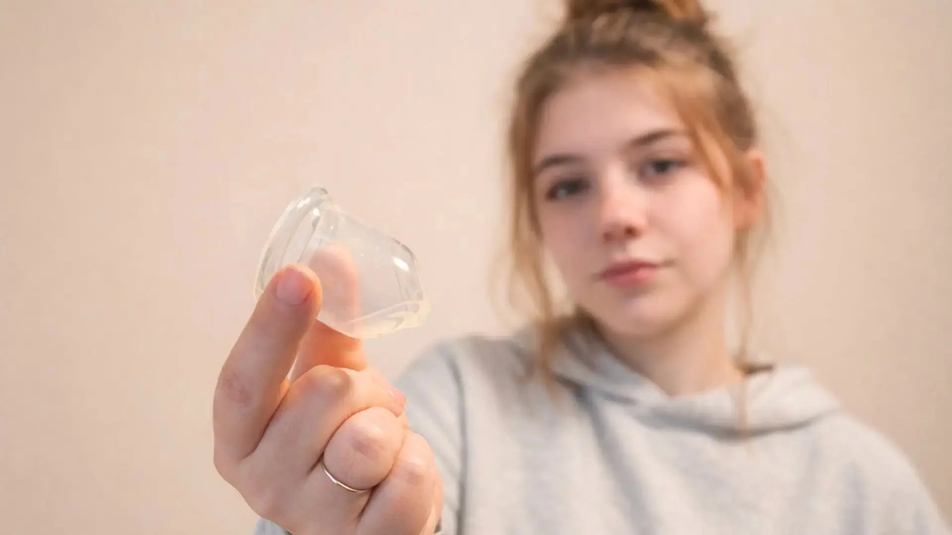 Jeune femme tenant une cup menstruelle transparente entre ses doigts, illustrant le choix d'une première protection.