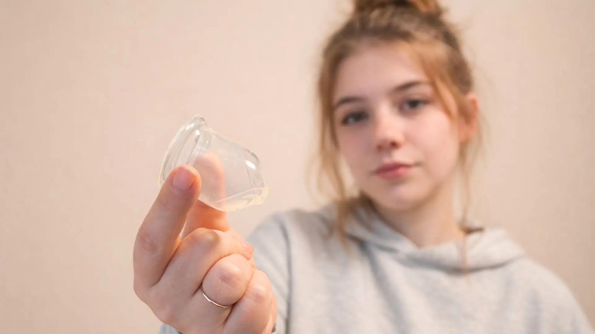 Jeune femme tenant une cup menstruelle transparente entre ses doigts, illustrant le choix d'une première protection. Bild